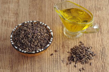 Milk thistle seeds and thistle oil in a glass gravy boat against a background of wood texture. Selective focus.