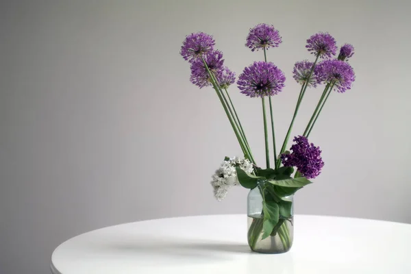 A bouquet of giant onion flowers and lilacs in a glass jar on a white round table. Selective focus.