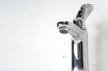 Beyaz arka planda bir damla su ile musluk. Su sızdırıyor ve tasarruf ediyor. Seçici odak.