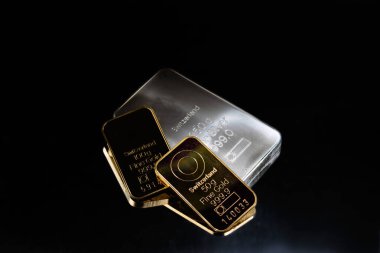 Gold and silver bars of various weights on a dark background. Selective focus.