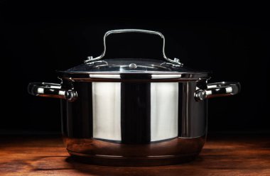 Yeni paslanmaz çelik bir tava, ahşap bir masada, siyah bir arka planda..