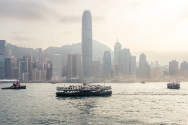 Hong Kong, 25 Mart 2019: Bulutlu bir günde, Hong Kong gökdelenleri ve Victoria Limanı 'ndaki yıldız bulvarından gelen geleneksel tekne manzarası