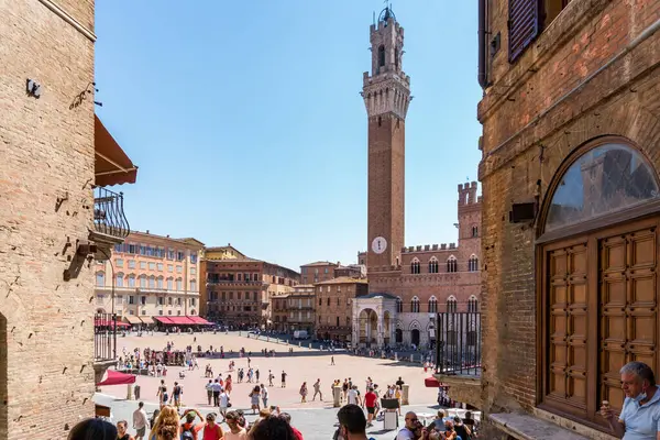 Siena, İtalya-Ağustos 10, 2020: İnsanlar ve turistler güneşli bir günde ünlü Piazza del Campo ve Torre del Mangia 'yı ziyaret ediyorlar