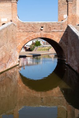 Comacchio, İtalya-2 Haziran 2023: İnsanlar güneşli bir günde Comacchio 'da ünlü üç köprünün önünde gezinirler.