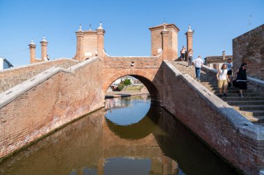 Comacchio, İtalya-2 Haziran 2023: İnsanlar güneşli bir günde Comacchio 'da ünlü üç köprünün önünde gezinirler.