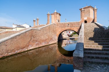 Comacchio, İtalya-2 Haziran 2023: İnsanlar güneşli bir günde Comacchio 'da ünlü üç köprünün önünde gezinirler.