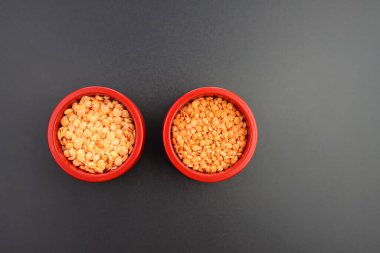 Kuru ve sırılsıklam kırmızı mercimekler gri arka planda yuvarlak kırmızı kâselerde. Sırılsıklam baklagiller. 