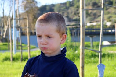 Kısa saçlı, sarışın çocuk yanaklarını şişirdi ve gözlerini aşağı indirdi. Beş yaşında somurtkan bir çocuk.. 