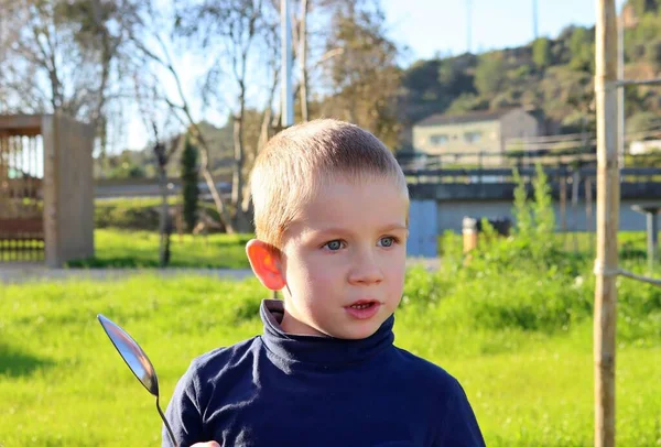 手に大きなスプーンを持った短髪の金髪の少年が不思議そうに目を背けている 驚くべき5歳の少年 — ストック写真