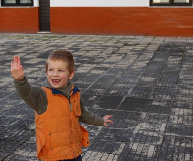 Sarışın çocuk gülümser ve elini ileri uzatır. Neşeli beş yaşında bir çocuk..