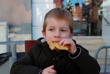 Sarışın çocuk bir kurabiyeden bir ısırık alır ve ilgiyle uzaktan bakar. Beş yaşındaki bir çocuğun sokak kafesinde atıştırmalığı var..