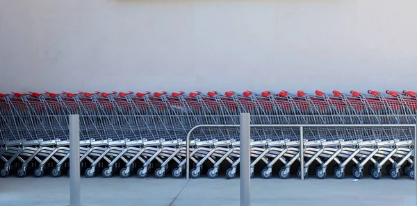 灰色の壁の背景の近くのスーパーマーケットの近くの空の金属製のカートの行 — ストック写真