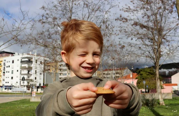 金髪の少年は目を細めて微笑んだ手にクッキーを持って — ストック写真