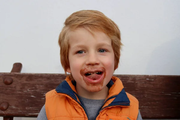 A blond boy with a dirty mouth and a sly smile. Playful five year old boy.