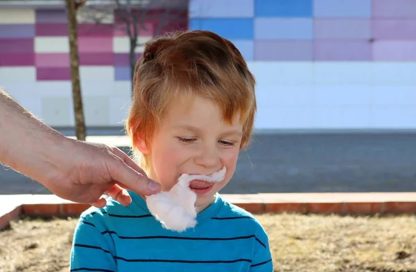 金髪の少年は父親の手から綿菓子を食べる 5歳の少年がお菓子を食べます — ストック写真
