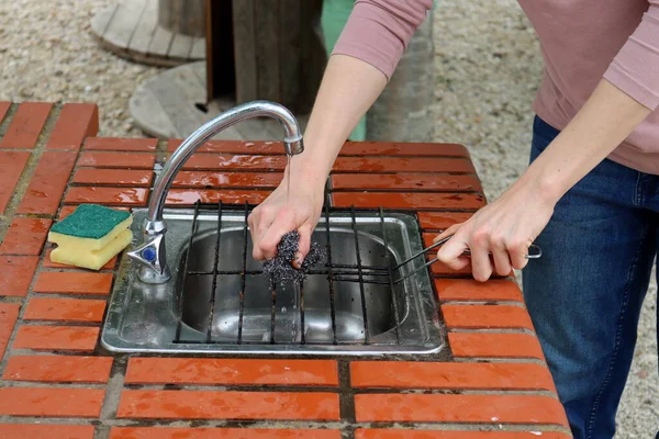 女性の手は金属スポンジでグリルグレートを洗う — ストック写真