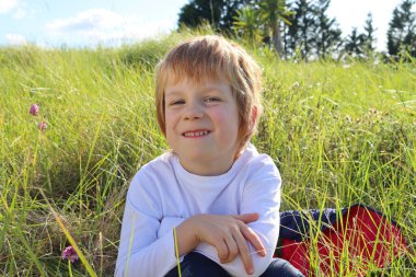 Sarışın çocuk alt dudağını ısırdı ve doğrudan kameraya gülümseyerek baktı. Flört eden altı yaşında bir çocuk..