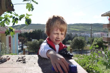 Sarışın bir çocuk evin terasında oyuncak bir arabayla oynuyor. Duygusal 6 yaşındaki çocuk..