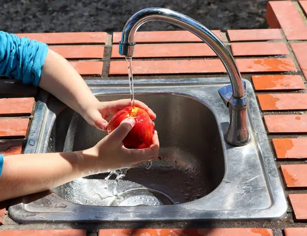 子供の手は開いたキッチンで蛇口の上に赤いネクタリンを洗います 選択的なフォーカス — ストック写真