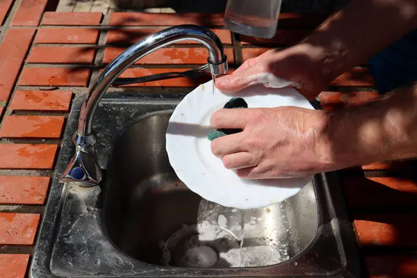 A man washes a dirty plate in the kitchen sink, close-up of his hands. Washing dishes in an open kitchen.