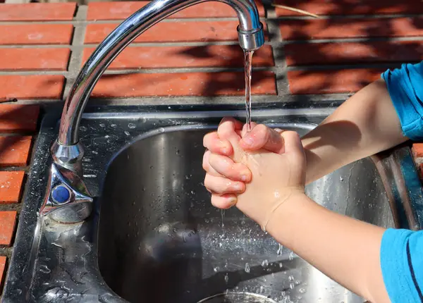 子供は彼の指を横切って キッチンシンクの水の下でそれらを洗います ロイヤリティフリーのストック写真