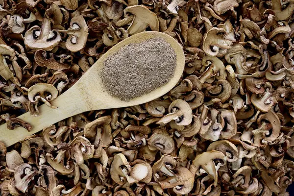 Kuru mantarların arka planında tahta kaşıkta mantar tozu..