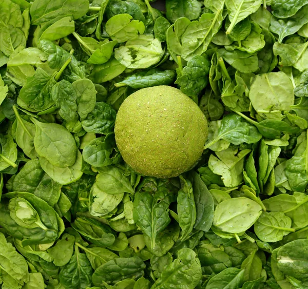A circle of green dough against a background of fresh spinach leaves. Spinach dough