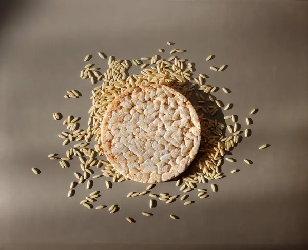 Round rice cracker with scattered rice grains on gray background, top view
