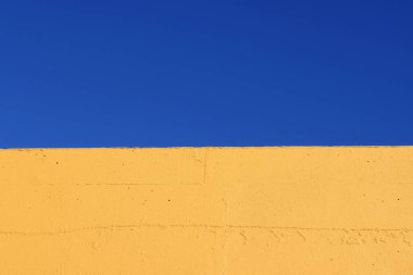 Mavi gökyüzüne karşı sarı duvarın bir parçası. Mavi ve sarı, iki parçaya bölünmüş.