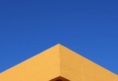 Sarı duvarın köşesi mavi gökyüzü arkaplanına karşı simetrik görünümde, geometrik dış mimari minimal stilde. Bir binanın ayrıntısı