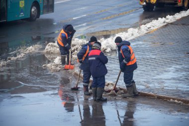 Uralsk, Kazakistan (Kazakistan), 28.02.2023 - Turuncu yelekli yol bakım işçileri kürekle kar temizliyor. Kürekli işçiler şehir merkezindeki sokaktaki karları temizliyor..