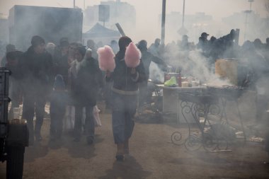 Uralsk (Oral), Kazakistan, 22.03.2024 - Kazakistan 'da Nauryz tatili. Pamuk şekerli bir kız tatil boyunca barbeküden çıkan dumanda yürür..