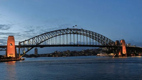 シドニー港橋は夕暮れ時に ポート ジャクソンの南岸にあるオペラ ハウスから東から西に見えるように国旗が上に振ってある ほとんど澄んだ空の下で洪水になった Nsw Australia — ストック写真
