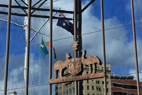 Reflections on the glass wall housing the entrance to the Australian National Maritime Museum: national-aboriginal-Torres Strait islander flags, and buildings on Murray Street. Sydney-NSW-Australia.