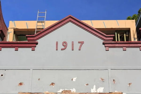 stock image Chipped facade of terrace house in Federation free style under restoration featuring red AD 1917 date, gray-painted wall, triangular parapet, on Ormond Street, Paddington suburb. Sydney-NSW-Australia.