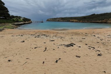 Port Campbell 'ın güneybatıya yönelik plajı, günbatımının başlangıcında bulutlu bir gökyüzünün girişindeki yerel balıkçı iskeletiyle birlikte kireçtaşı uçurumları arasında korunaklı bir körfezde. VIC-Avustralya.