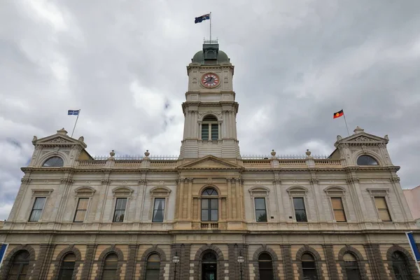 Two-story, Classical Revival style heritage Town Hall building: two-level central clock tower, pediment-ended lateral pavilions. National, aboriginal and Eureka flags waving. Ballarat-VIC-Australia.