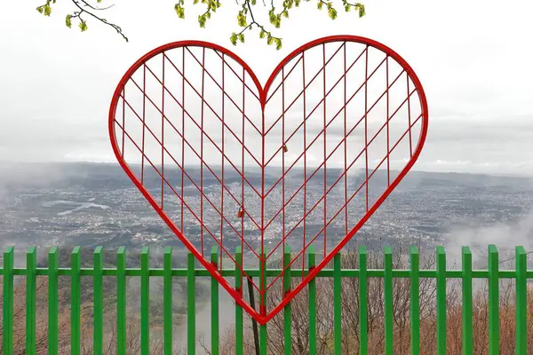 View from the Dajti Balcony-Ballkoni Dajtit towards the southwest to the whole capital area across a red-painted, heart-shaped metal mesh welded to a green-painted open fence. Tirana-Albania.