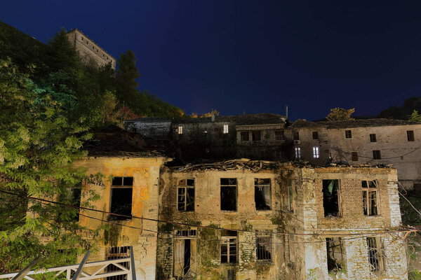 Night photography under a starry sky of the rear of old townhouses along Rruga Gjin Bue Shpata and the remains of ruined houses at the foot of the hill housing the local fortress. Gjirokaster-Albania.