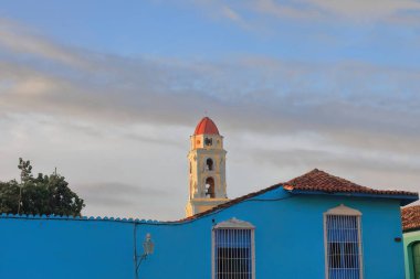 Trinidad, Küba-12 Ekim 2019: Eski İglesia de San Francisco de Asis Kilisesi 'nin kulesi Plaza Belediye Başkanı Meydanı' nın batı yakasındaki tek katlı bir evin gök mavisi duvarını aşıyor..