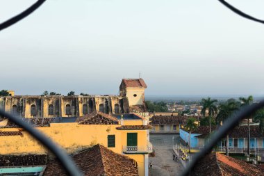 Trinidad, Cuba-October 12, 2019: Early sunset, SE-wards view from the San Francisco Church belfry over Cristo Street, Plaza Mayor Square, Brunet Palace, Holy Trinity Church, framed by a window railing clipart
