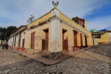 Trinidad, Cuba-October 13, 2019: Dilapidated, chipped facade of colonial style, one-storey building at the Calle Alameda and Calle Cristo Streets northeast corner painted in peach-yellow-orange colors clipart