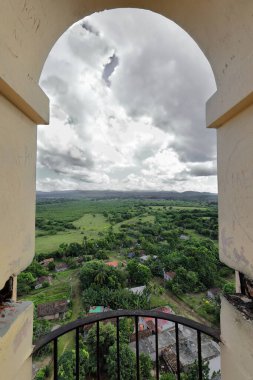 Eastward, high-angle view framed by a round arch on the uppermost level of the Manaca Iznaga tower over the estate's farmland, forests, patchwork fields and the far Escambray Mountains. Trinidad-Cuba. clipart
