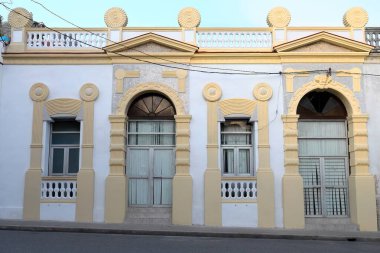 Camaguey, Küba-15 Ekim 2019: Art-deco unsurları, parşömenleri, disk akroterisi, kemerler, pedikürleri içeren eklektik stil koloni evi cephesi, Tarih Merkezi bölgesinde eğimli bir sokağa bakıyor.