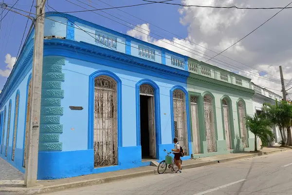 stock image Bayamo, Cuba-October 16, 2019: Renewed row of eclectic, one-storey, colonial style houses on Calle CM.Cespedes Street north side, corner with Avenida Perucho Figueredo Avenue. Cyclist boy at the door.