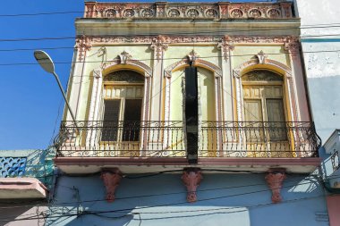 Santiago, Küba, 20 Ekim 2019: 1900 'lerin başında, iki katlı, eklektik tarzda binaların güneye bakan ön cephesi, açık sarı birinci kat, pembe pervazlı, tam uzunluktaki balkonda demir parmaklıklar..