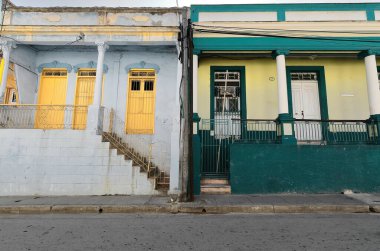 Santiago, Küba-20 Ekim 2019: Clarin-Padre Quiroga Caddesi 'ndeki Koloni tarzı evlerin batıya bakan cephelerinde soluk mavi ve limon sarısı duvarlar, beyaz ve çarpıcı sarı kapılar ve pencereler