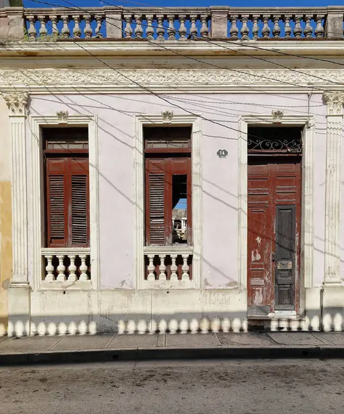 Stock image Santiago, Cuba-October 20, 2019: Pale pink wall with white mouldings, chipped maroon-red wood door and window shutters, east-facing facade of uninhabited, dilapidated Eclectic building, Clarin Street.