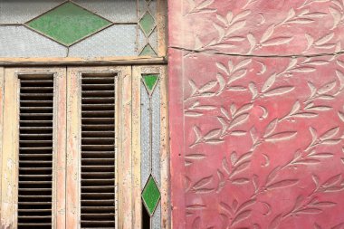 Decoration detail of an Eclectic style house on Calle Amargura Street with a rose-red colored, vegetable-leaf carved wall contrasting with a window of louver-shutter, green and colorless glass frame. clipart