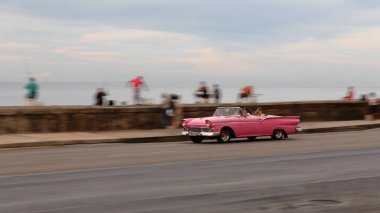 Havana, Küba-26 Ekim 2019: Pembe klasik Amerikan arabası -Ford Fairlane 500 üstü açık 2 kapı 1957 'den doğudan batıya Malecon gezinti güvertesinde yerel balıkların dinlenip sohbet ettiği.